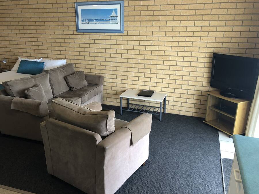 Ein Hotelzimmer mit einer Ziegelwand, einem gerahmten Bild, einer Couch, einem kleinen Tisch mit einem Tablet und einem Fernseher auf einem Holzboden.