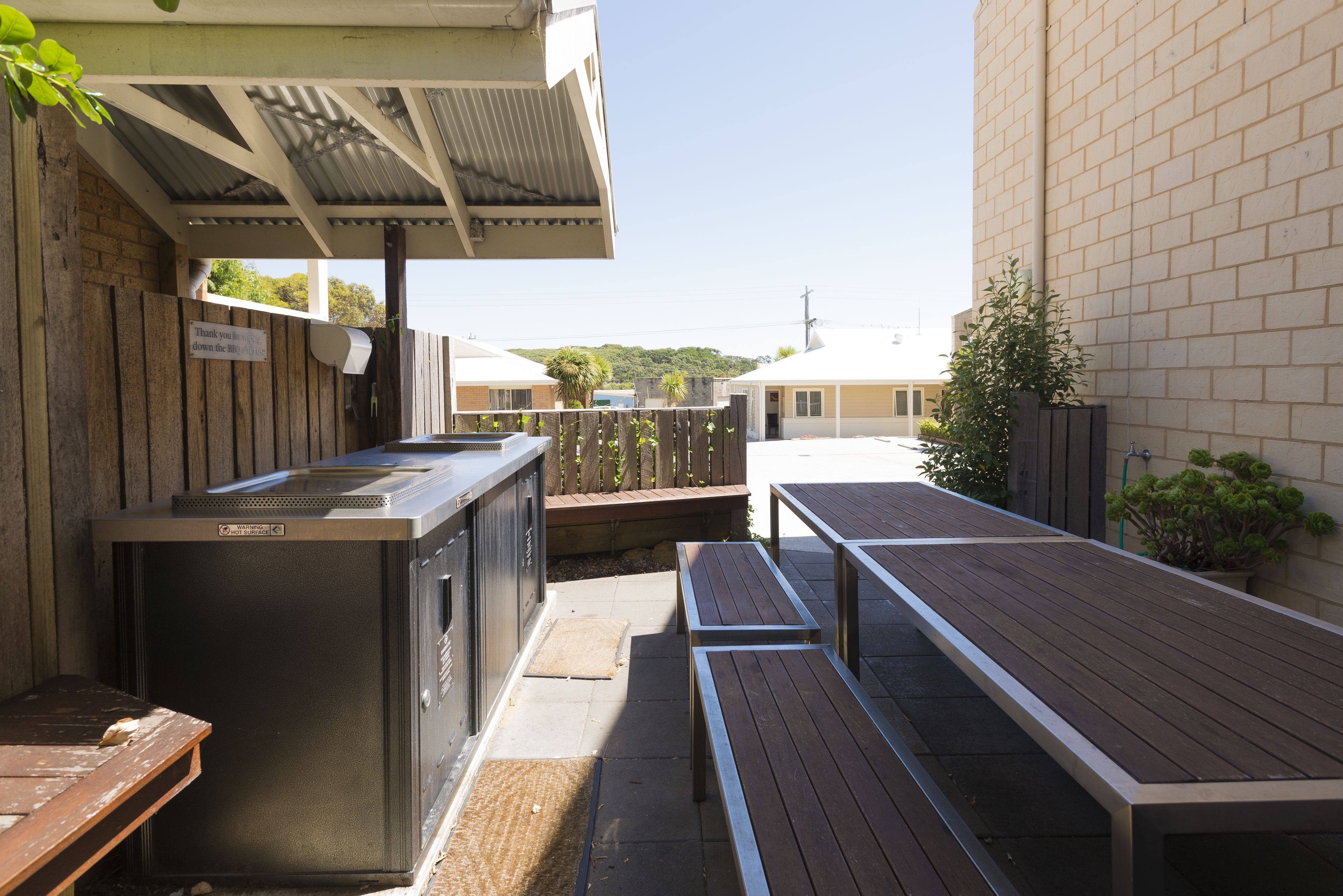 A covered outdoor area with a barbecue grill, wooden benches, and a brick wall.
