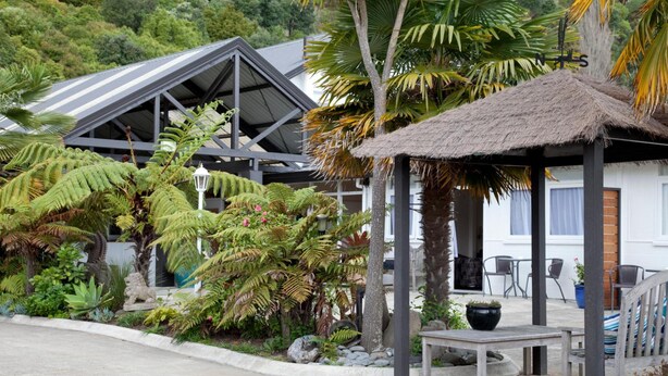 Ein tropisches Resort mit einem strohgedeckten Pavillon, einer überdachten Außenlounge und üppiger Vegetation.