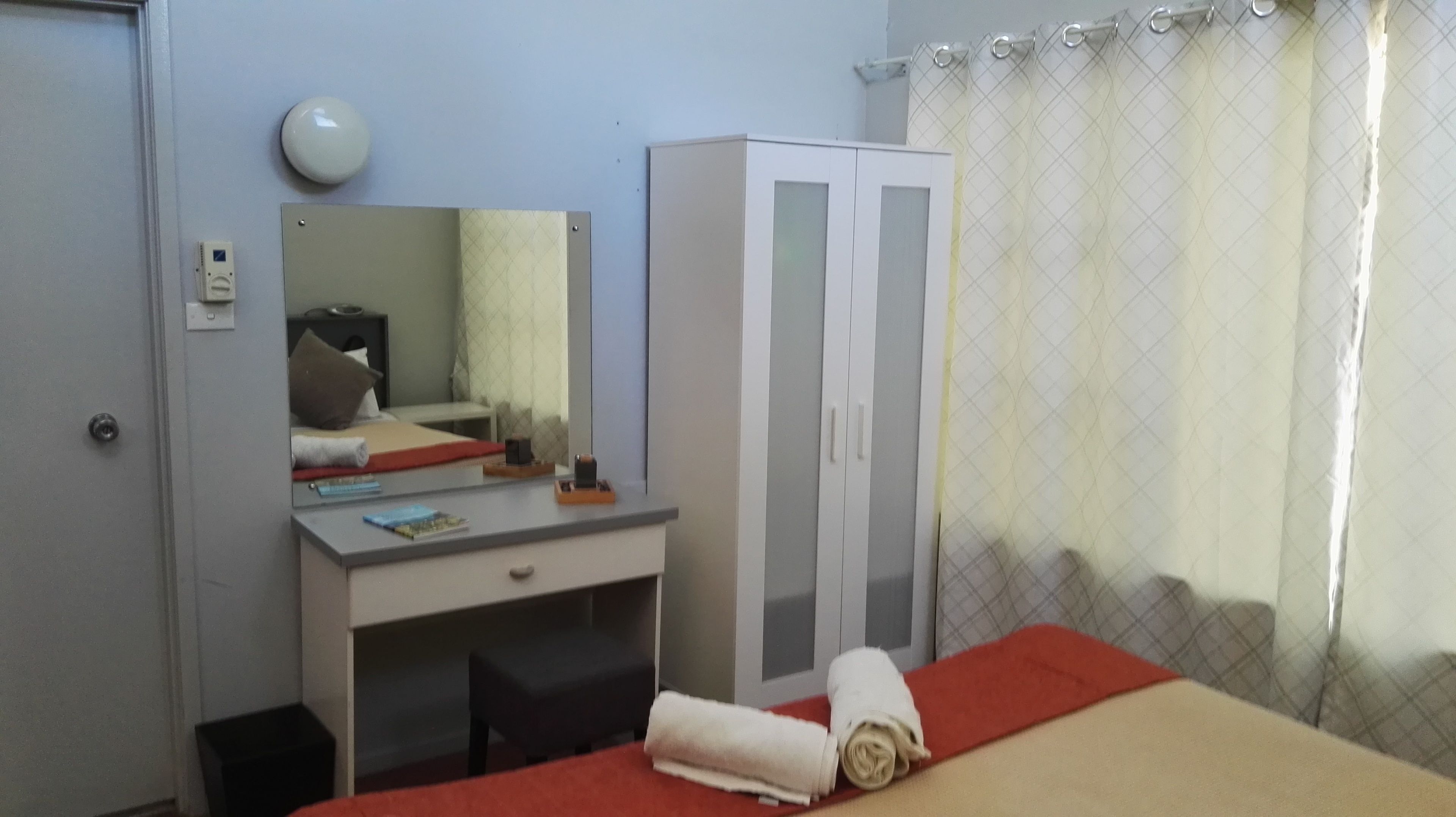 Una habitación de hotel con cama, escritorio, armario, espejo y cortina.