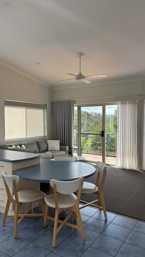 A modern living room with a round table, chairs, a sofa, and a ceiling fan. - Bluewater Apartments Merimbula (Merimbula)