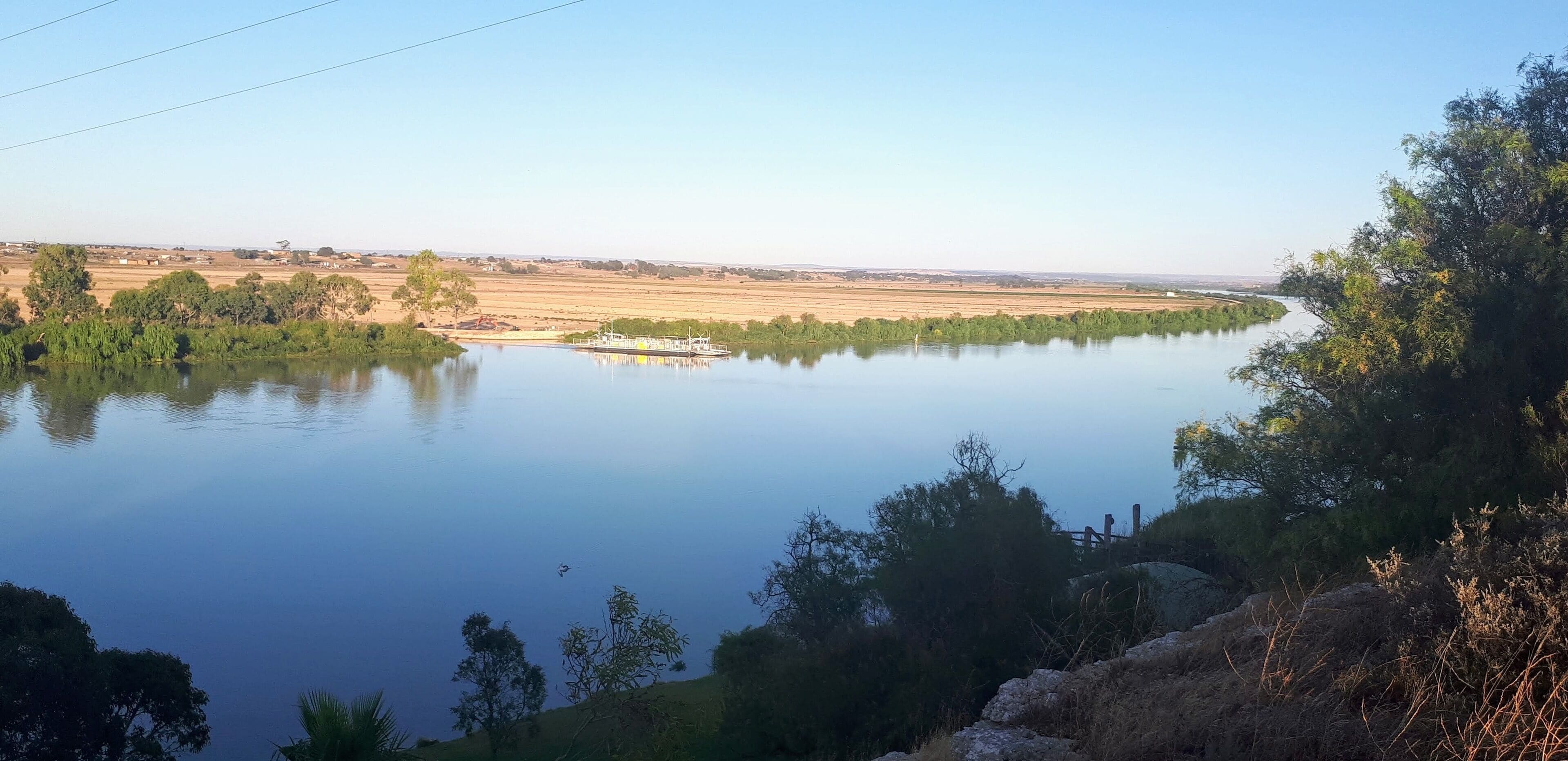 Un río tranquilo con un puente y árboles en primer plano.