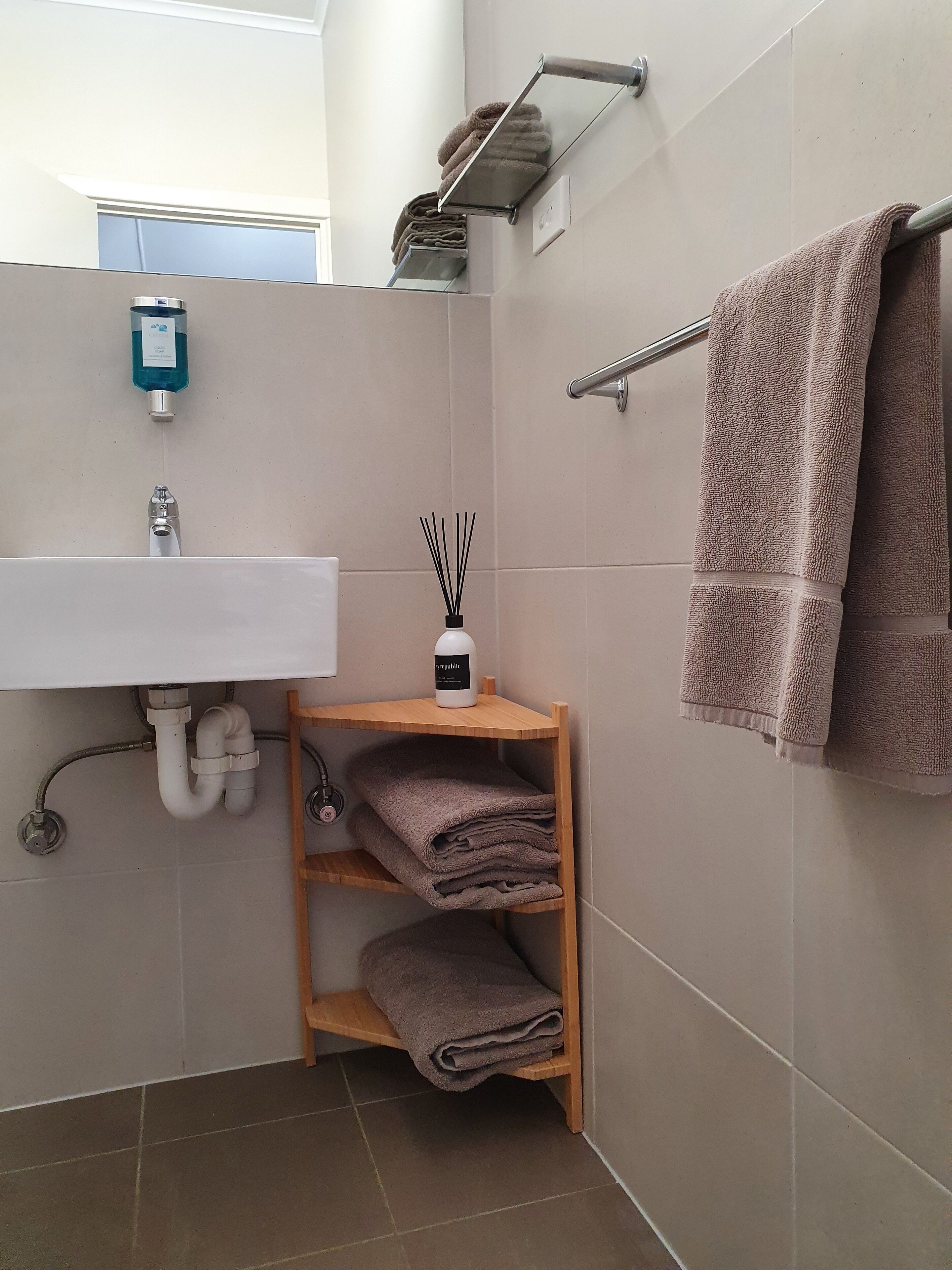 Un bagno con lavandino, specchio, porta asciugamani e uno scaffale con asciugamani piegati.