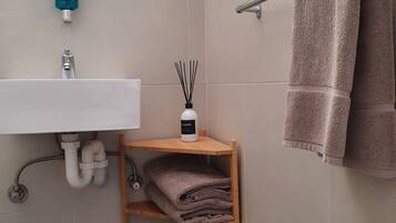 Un bagno con lavandino, specchio, porta asciugamani e uno scaffale con asciugamani piegati.