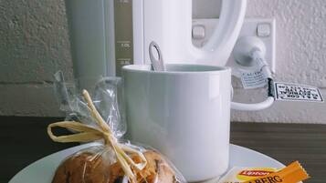 Una cafetera blanca, una taza, un plato con una galleta y paquetes de té Lipton sobre una mesa.