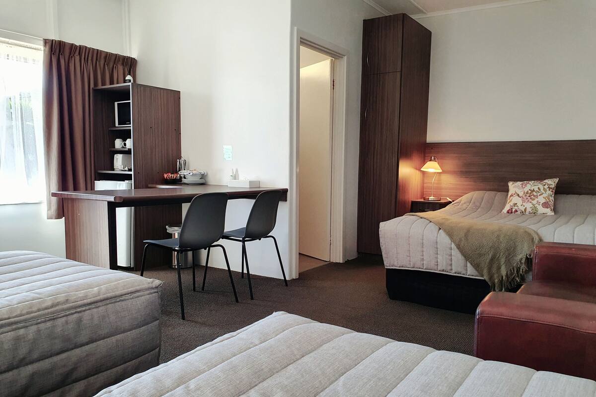 Habitación de hotel con cama, escritorio y silla, armario y mesita de noche con lámpara.