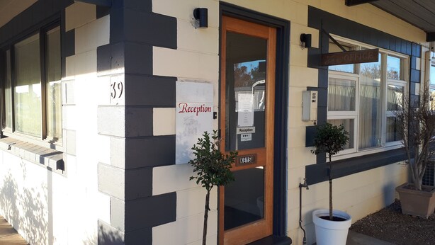A building with a reception area, a reception sign, a key box, and two potted plants.