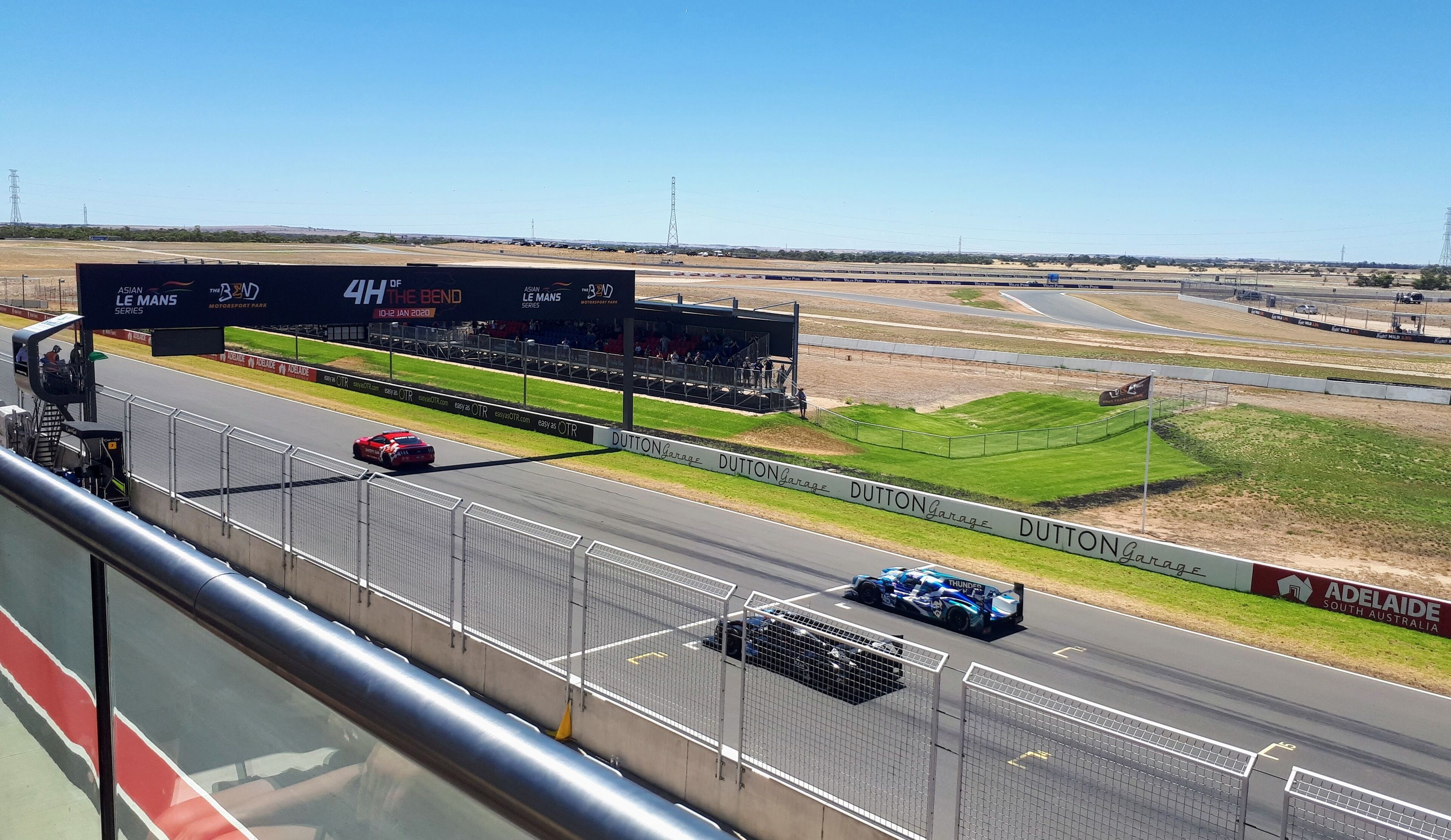 A race track with multiple cars, a large electronic scoreboard, and advertising banners.