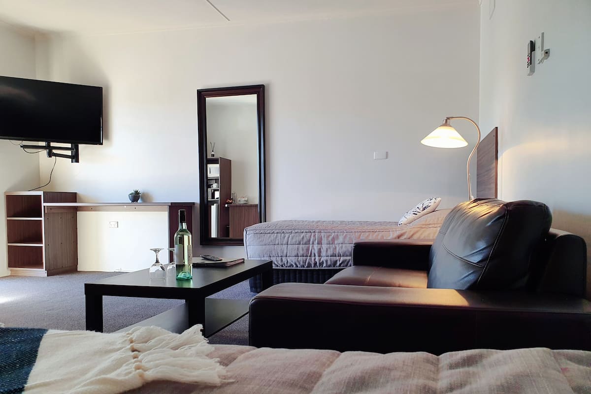 Una habitación de hotel moderna con cama, sofá, escritorio, televisión y espejo.