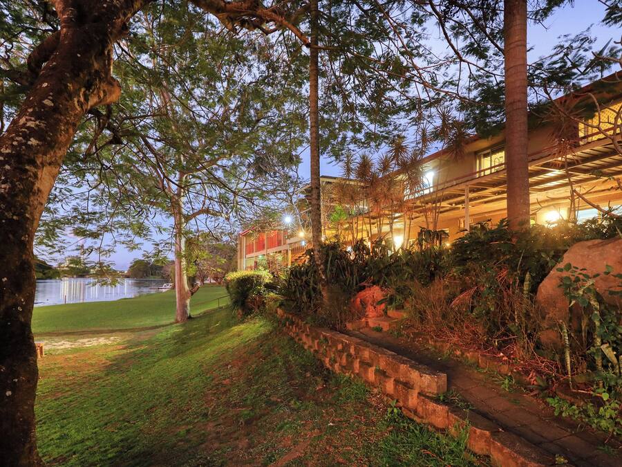 A lakeside hotel with a well-maintained lawn, stone steps leading to the entrance, and a view of the lake.