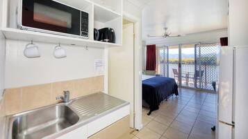 A compact hotel room with a kitchenette, a balcony with a view, and a bed.