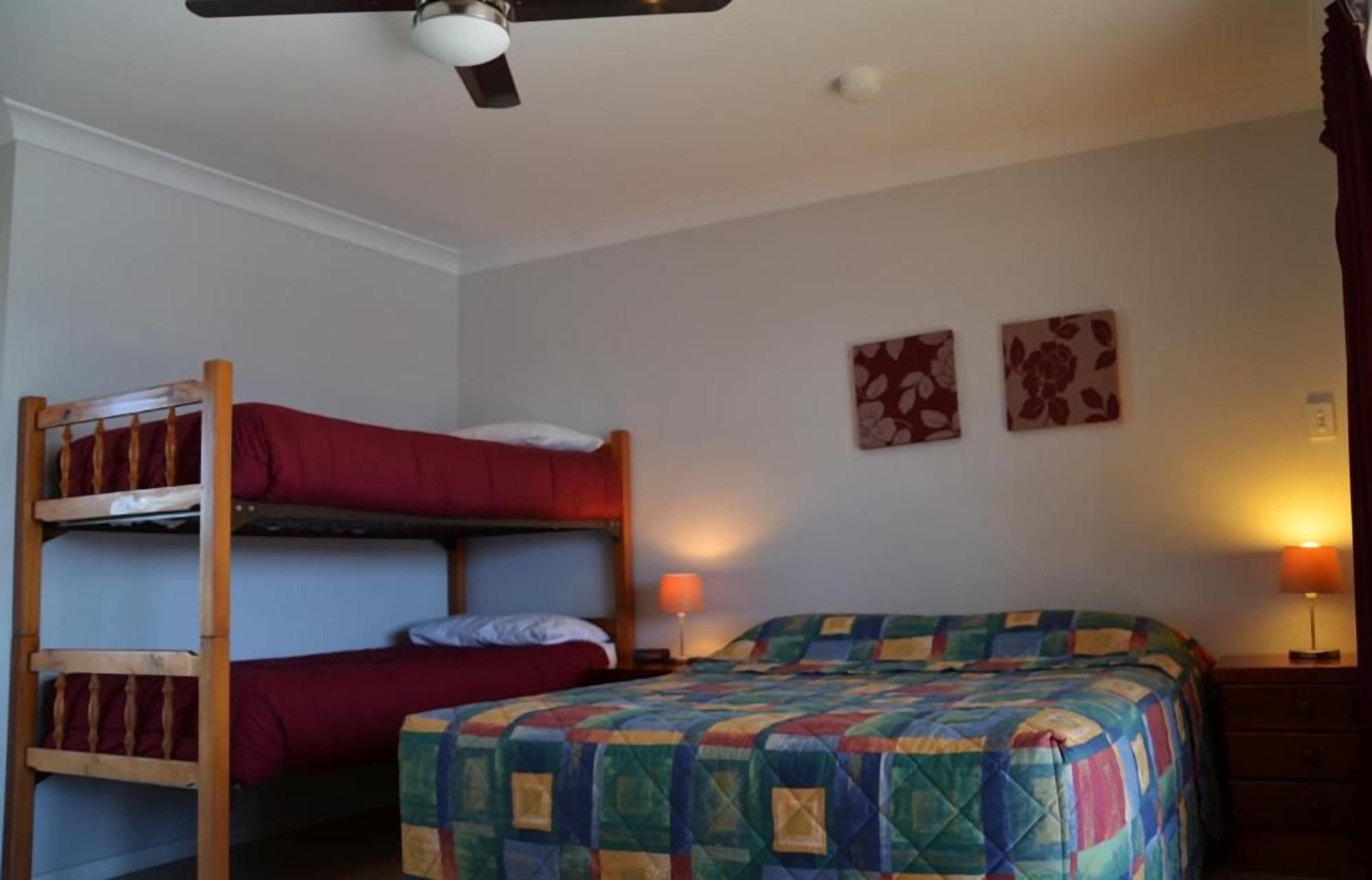 A room with bunk beds, a single bed, two wall-mounted lamps, and two wall-mounted floral artwork pieces.