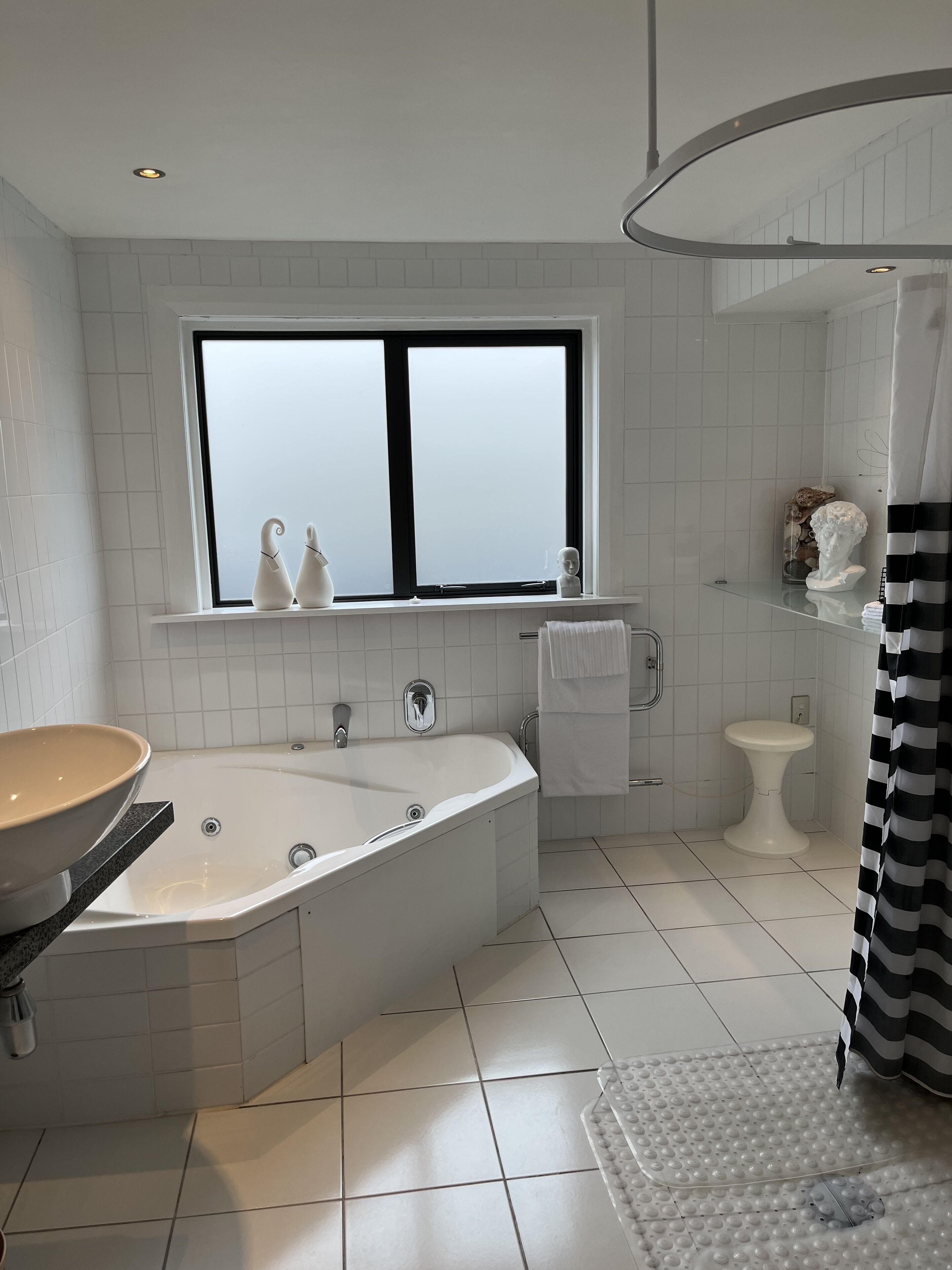 A modern bathroom with a freestanding bathtub, a window with frosted glass, a toilet, and a shower area.