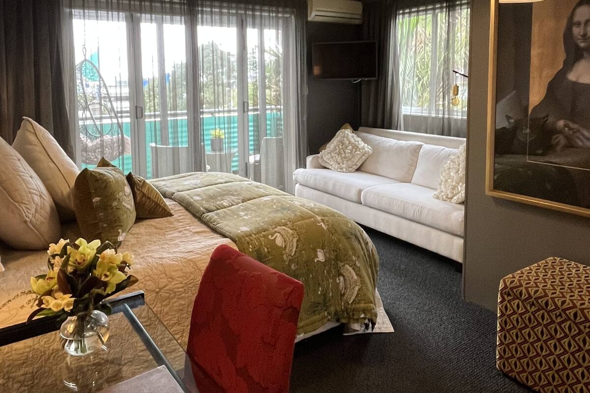 A hotel room with a bed, a sofa, a dining table with a vase of flowers, and a painting on the wall.