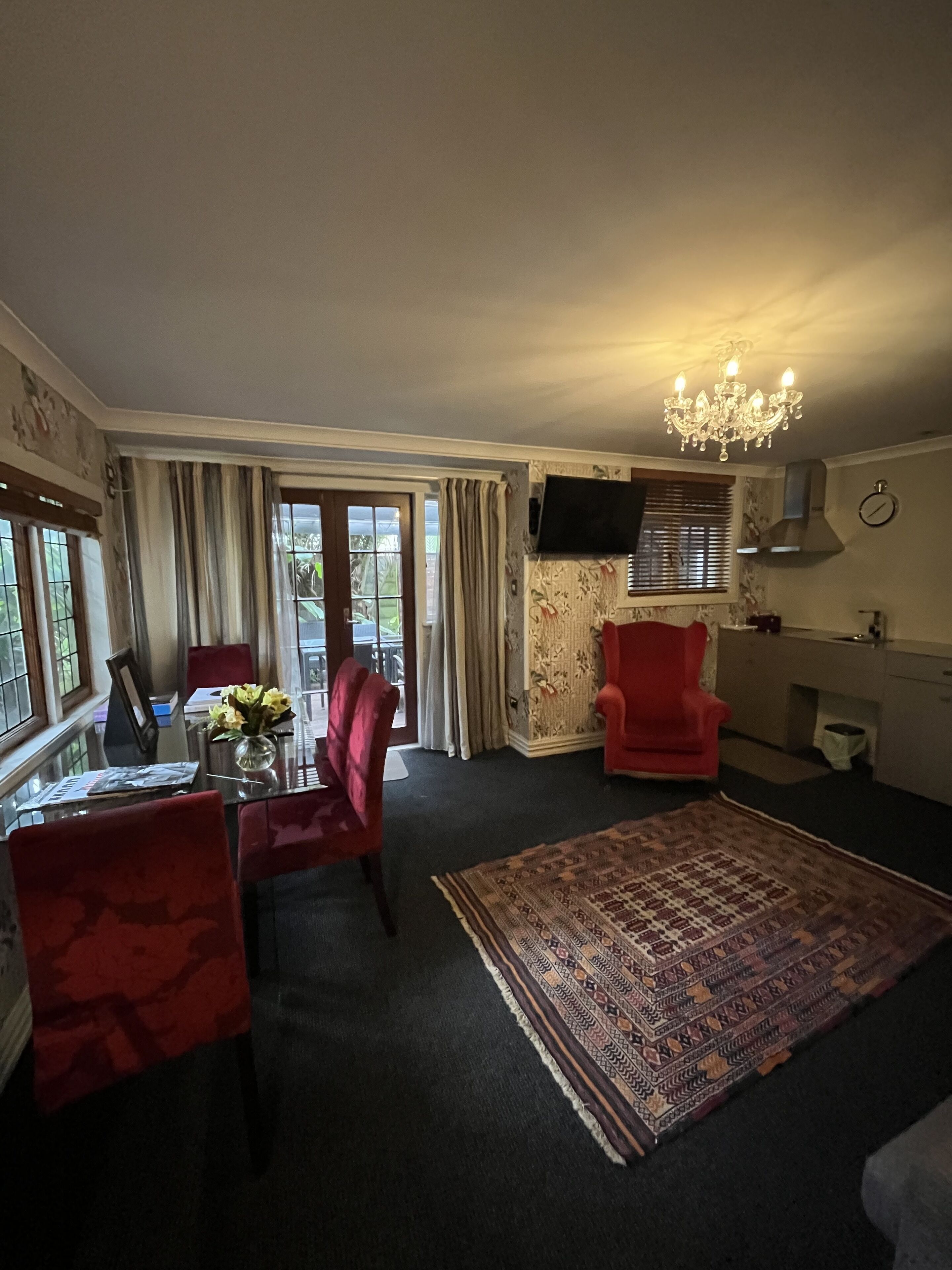 A living room with a dining area, a chandelier, a red armchair, and a patterned rug.