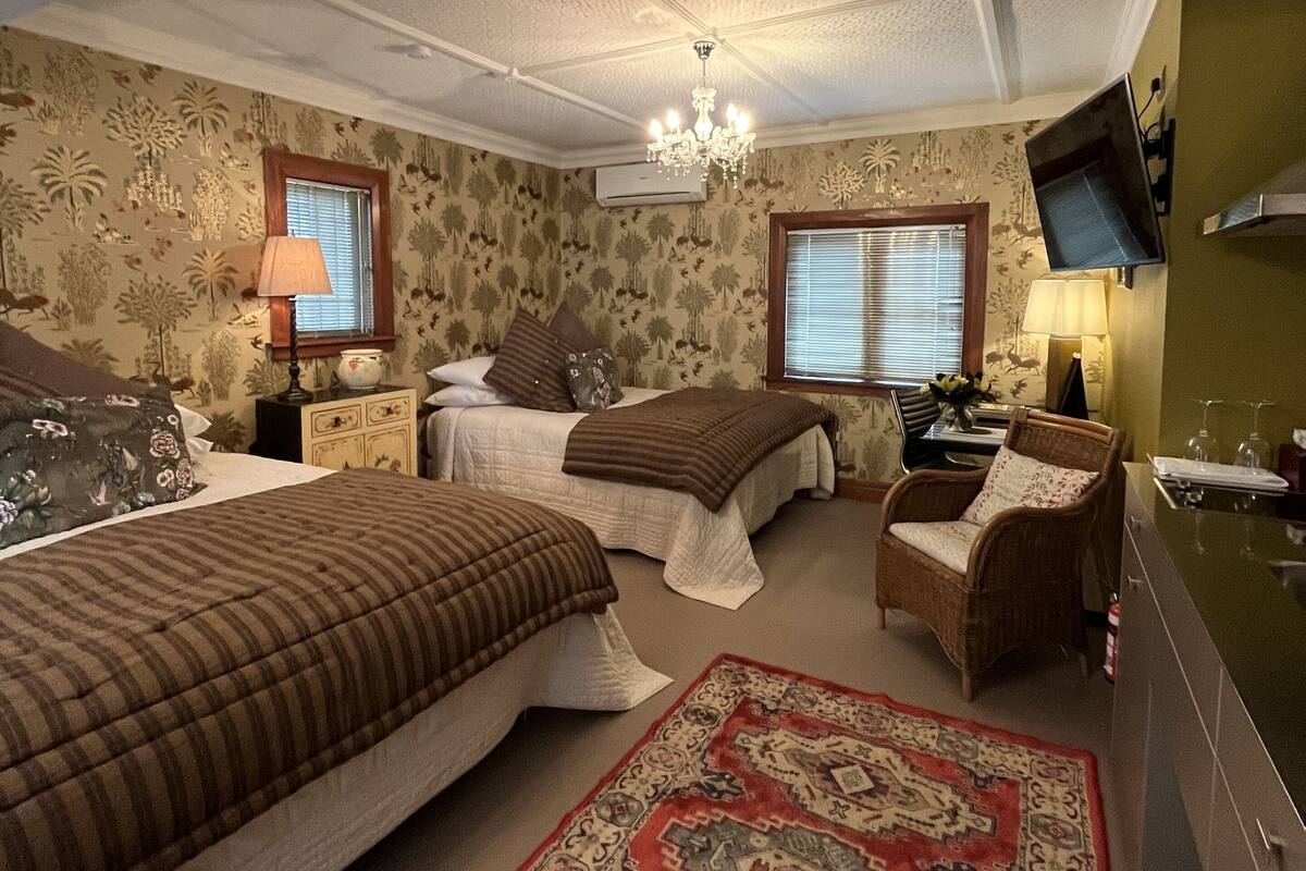 A bedroom with two beds, a chandelier, a television, and a red patterned rug.