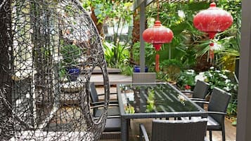 A glass-top table with wicker chairs, surrounded by a garden with red lanterns and a wire basket.