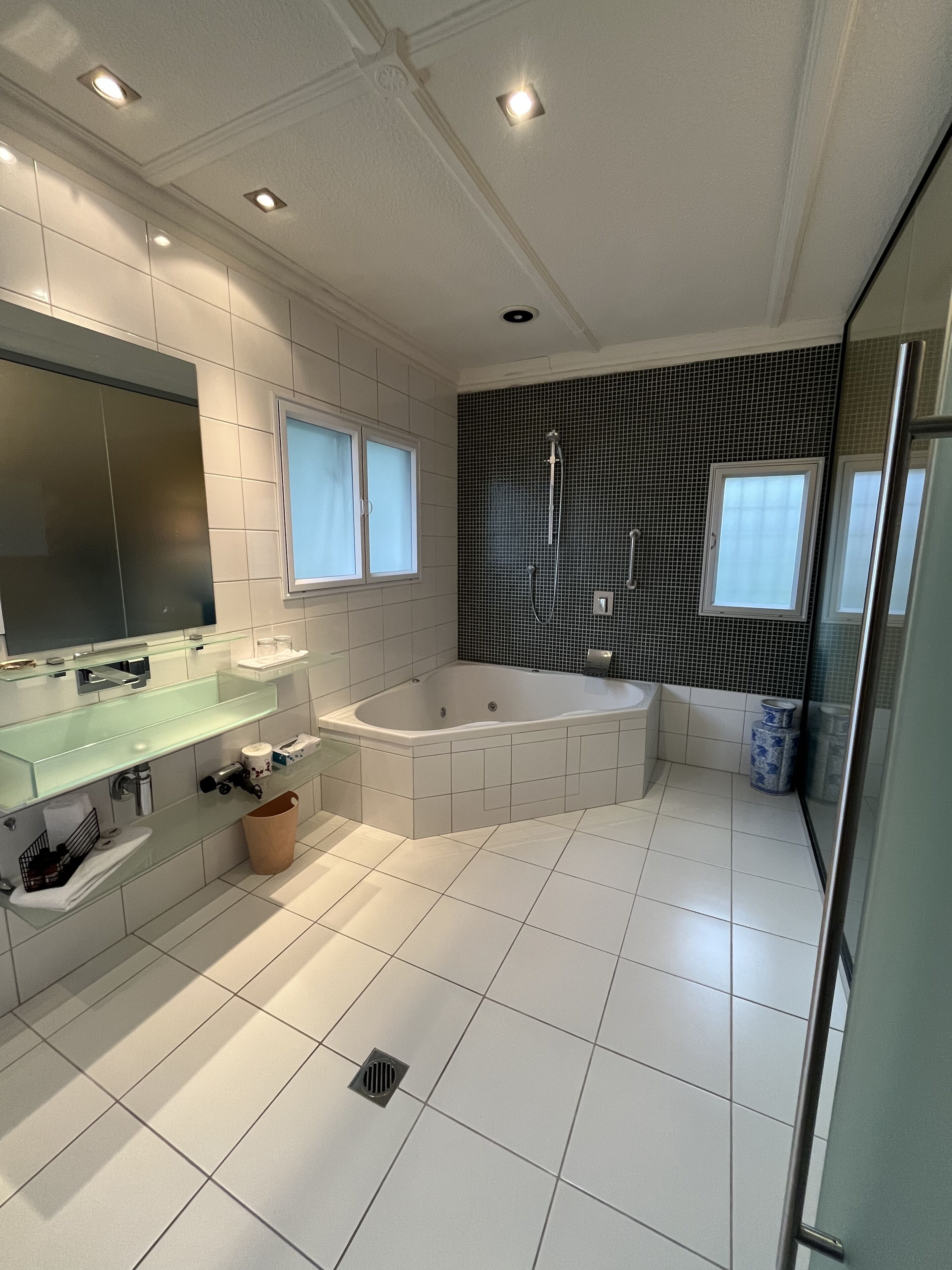 Un baño moderno con tocador con mampara de vidrio, un espejo grande, una bañera independiente y zona de ducha con pared de azulejos negros.
