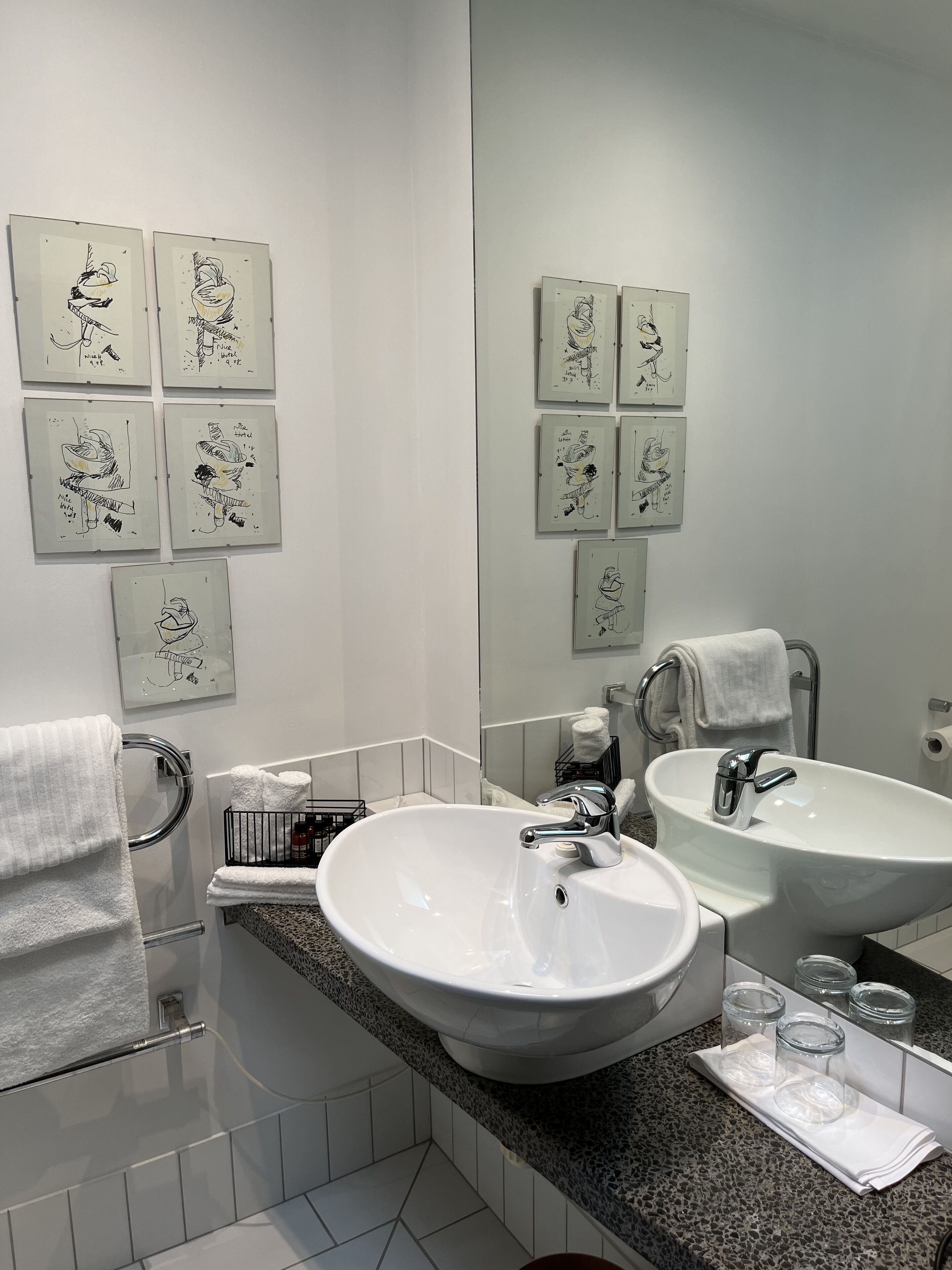 A modern bathroom with two sinks, a large mirror, and artwork on the walls.
