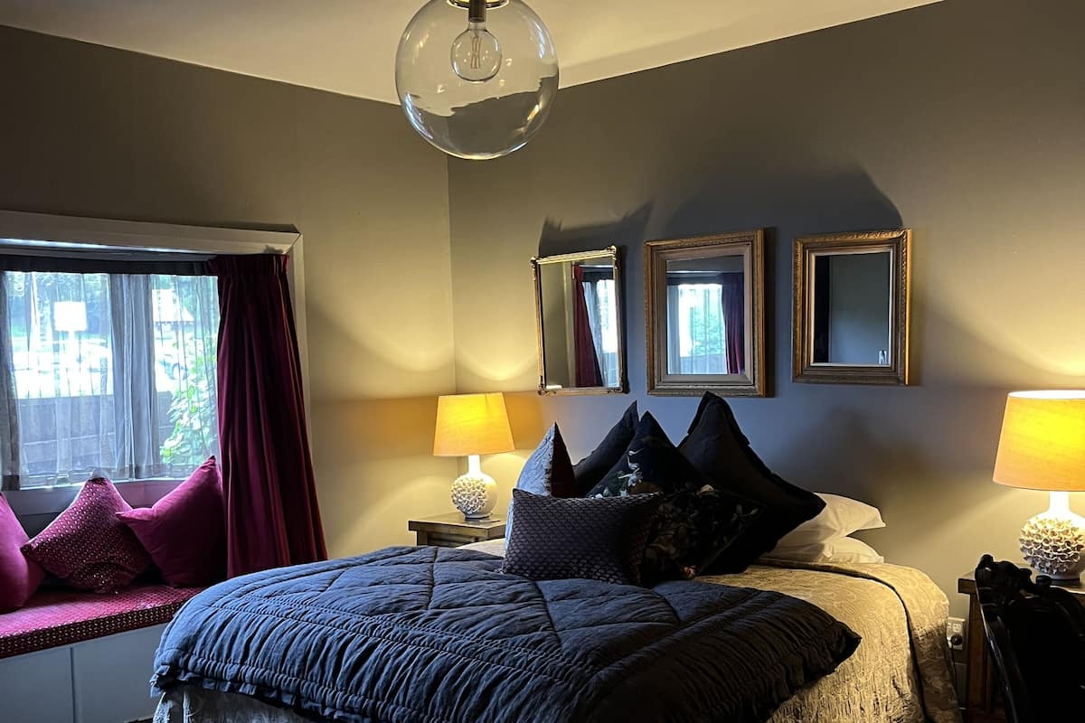 A bedroom with a large bed, two bedside lamps, a ceiling light, and a window with curtains.