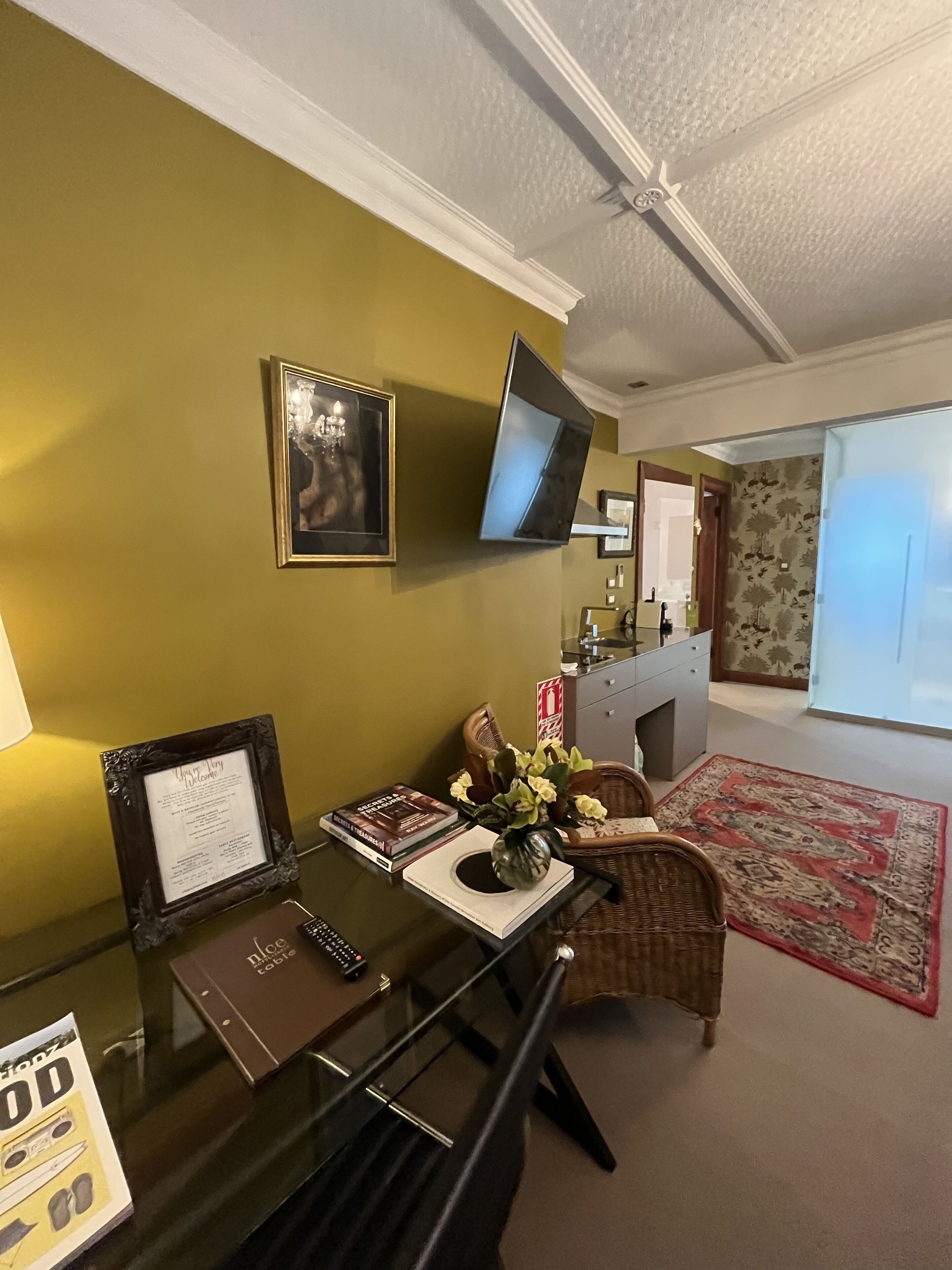 Un coin repas avec une table en verre, un panneau d’accueil décoratif et un téléviseur à écran plat fixé au mur.