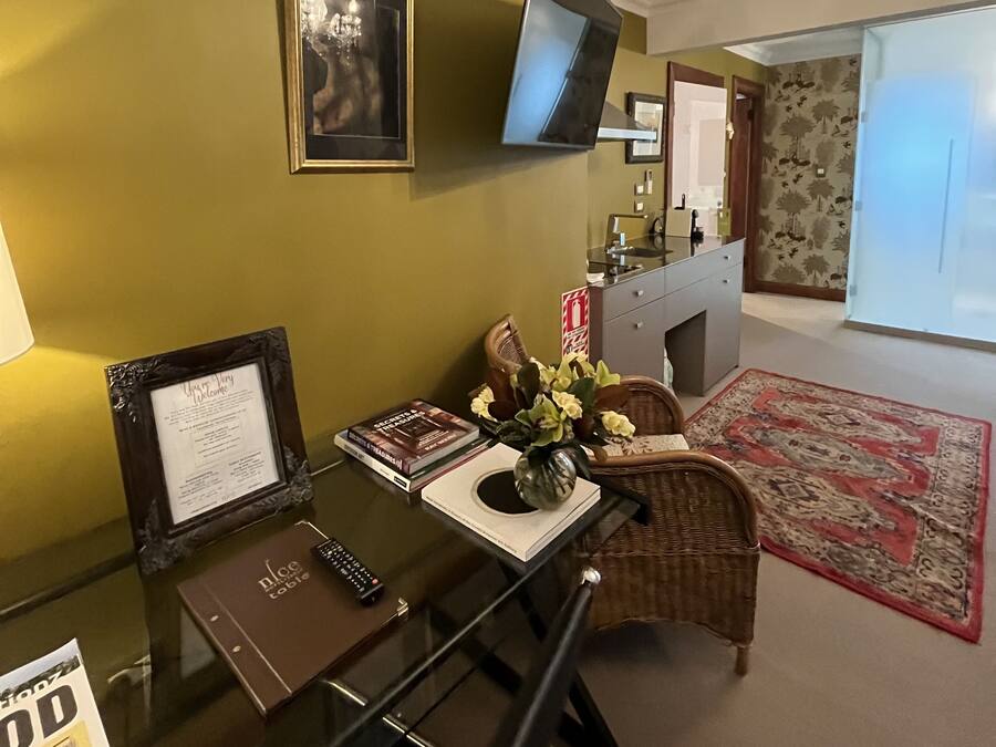 A dining area with a glass table, framed welcome sign, and a flat-screen TV mounted on the wall.
