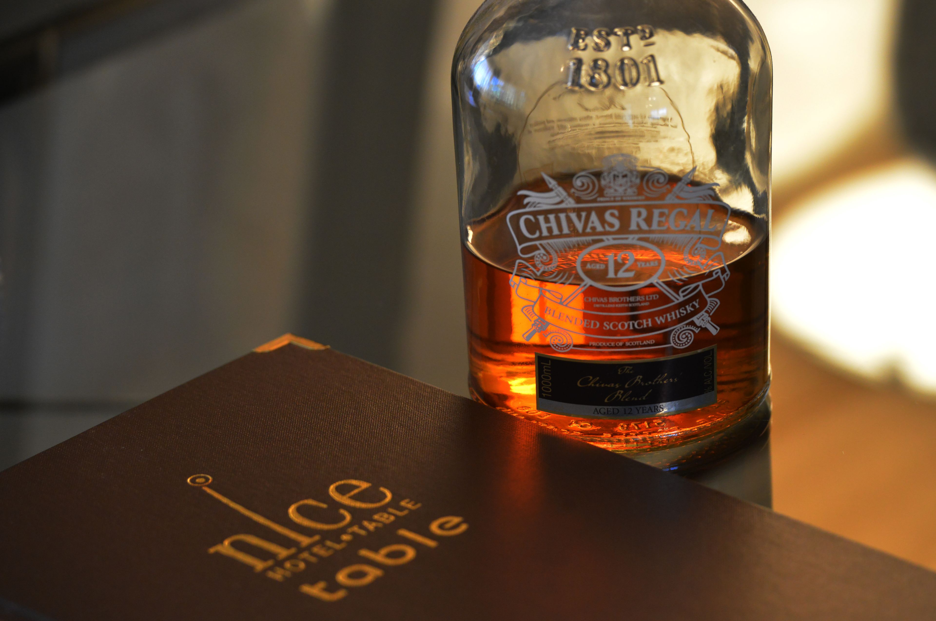 A bottle of Chivas Regal 12-year-old Scotch whisky on a table with a box labeled "nice table."