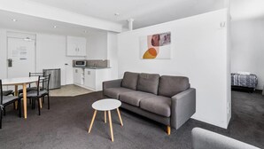 Una sala de estar moderna con un sofá gris, una mesa de centro redonda blanca y una cocina al fondo.