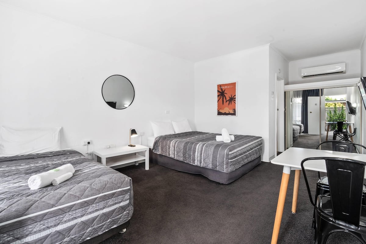 A hotel room with two beds, a desk, a chair, a mirror, and a picture of Hawaii.