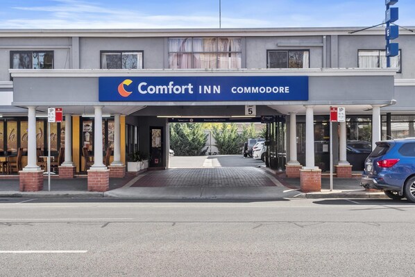 A Comfort INN commodore building with a covered entrance, columns, and a parking area.