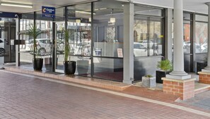 A hotel entrance with a reception desk, glass doors, and potted plants.