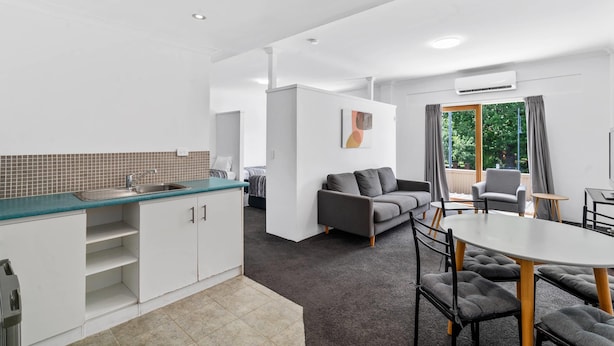Una habitación moderna y luminosa con cocina americana, una mesa de comedor con sillas, un sofá y un ventanal con cortinas.
