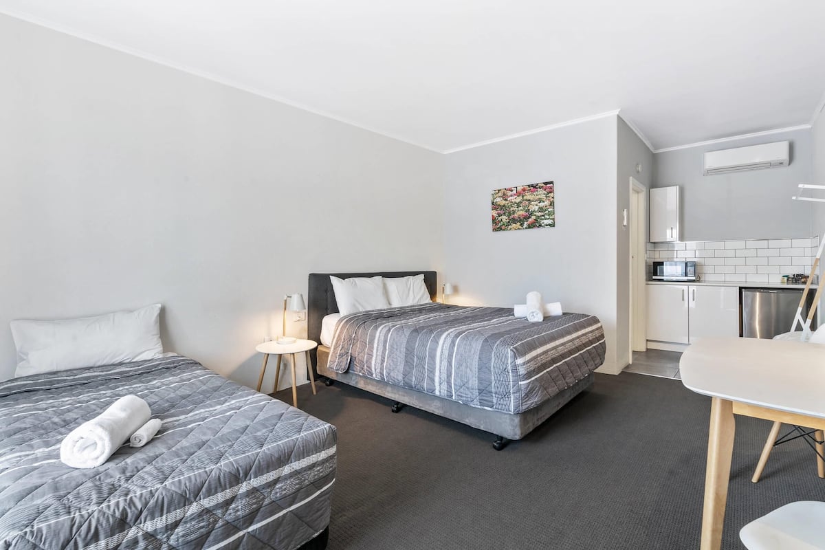 A hotel room with two beds, a small kitchenette, and a dining area.