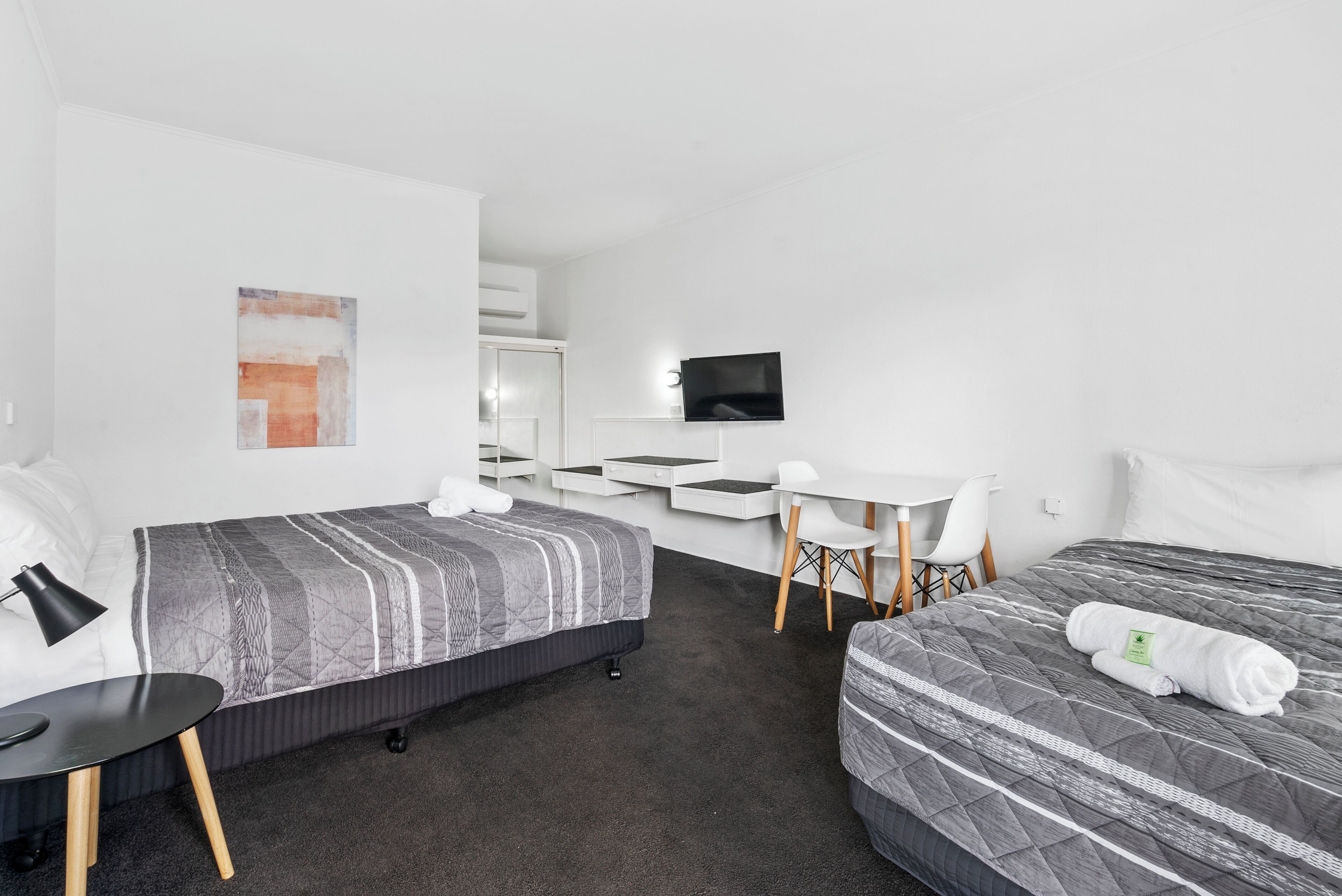 A modern hotel room with two beds, a desk, a chair, and a TV.