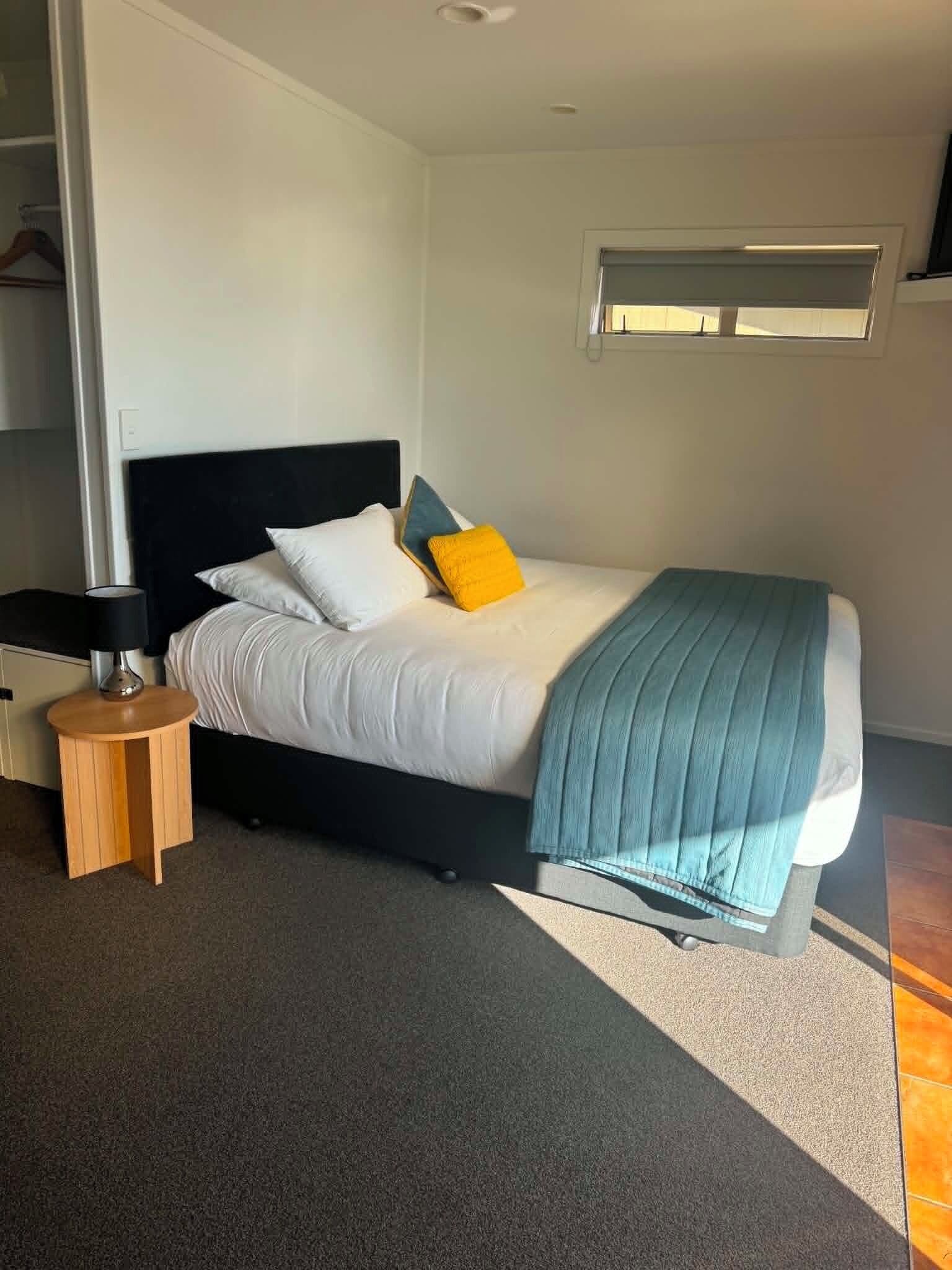A bedroom with a bed, bedside table, lamp, and a window.