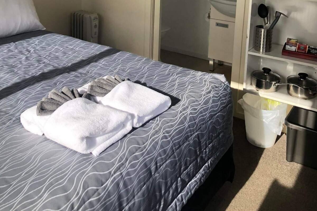 A hotel room with two beds, a window, a clock, and a kitchenette.