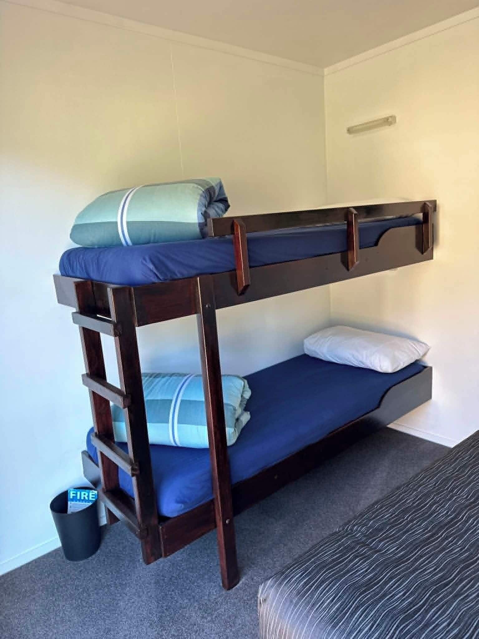 A bunk bed with a ladder, a small trash bin, and a patterned sofa.