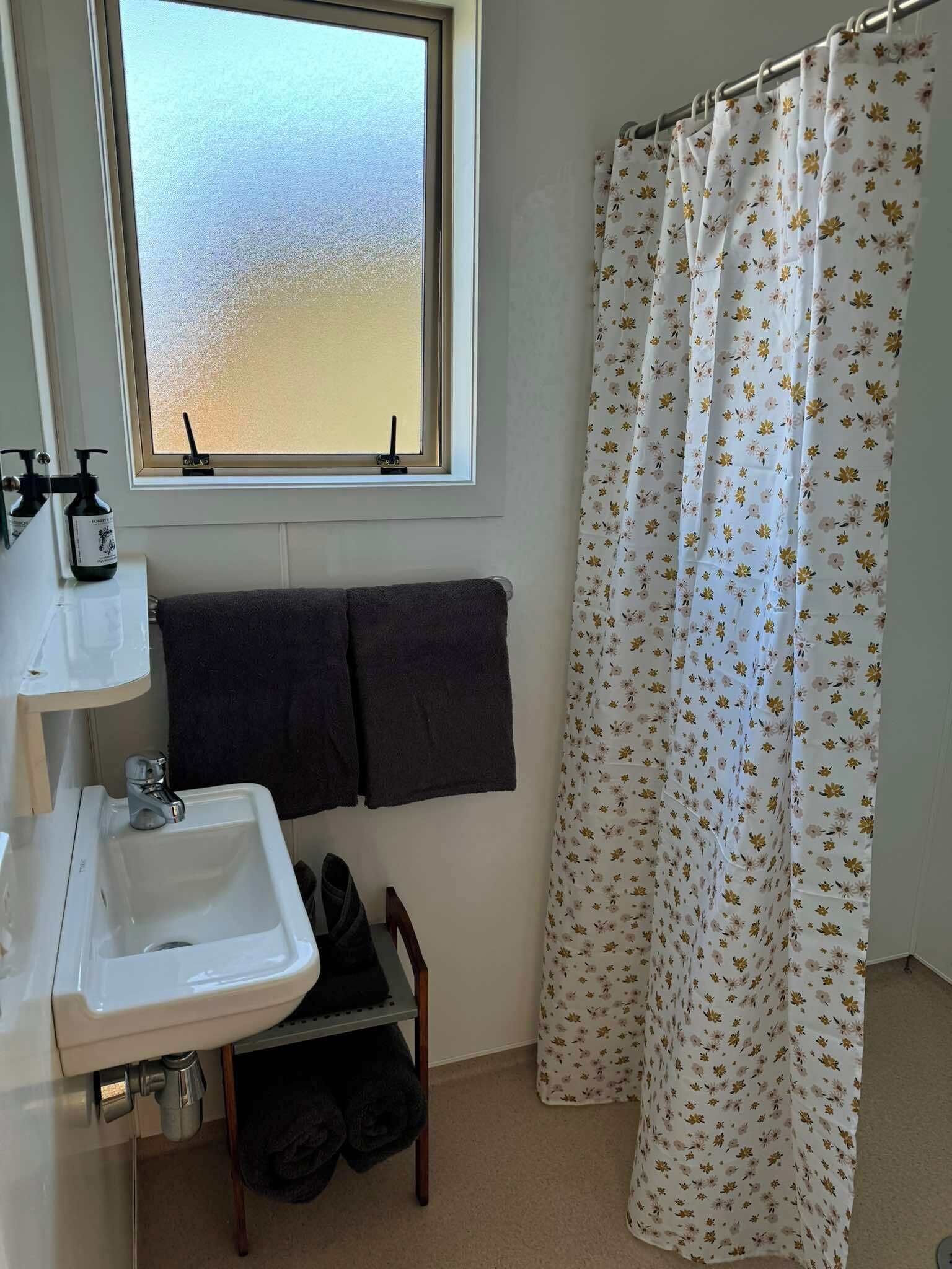 A bathroom with a window, a sink, a towel rack, and a shower curtain.