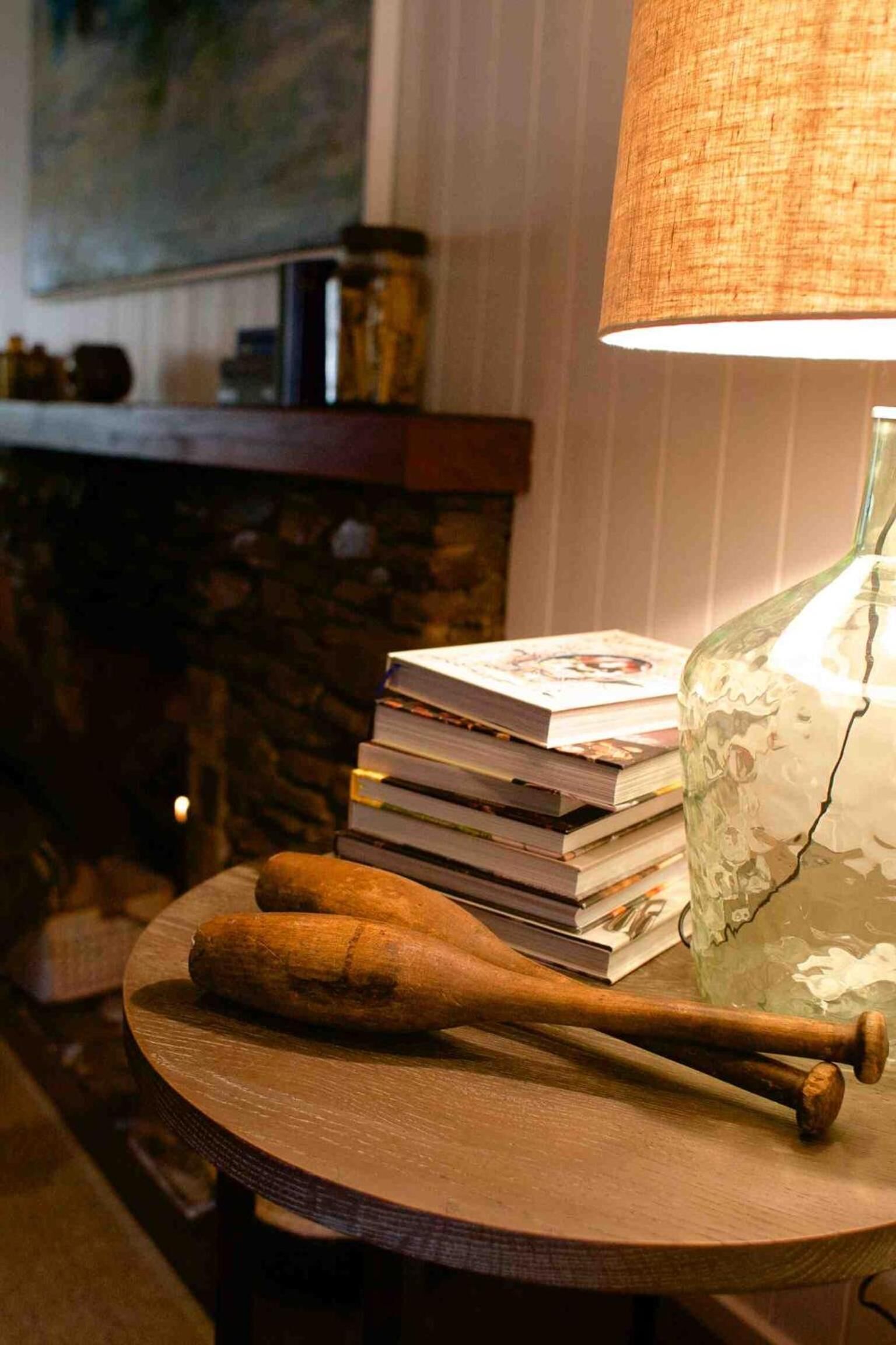A round wooden table with a stack of books, a glass bottle, and two wooden bats.