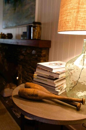 Una mesa redonda de madera con una pila de libros, una botella de vidrio y dos bates de madera.
