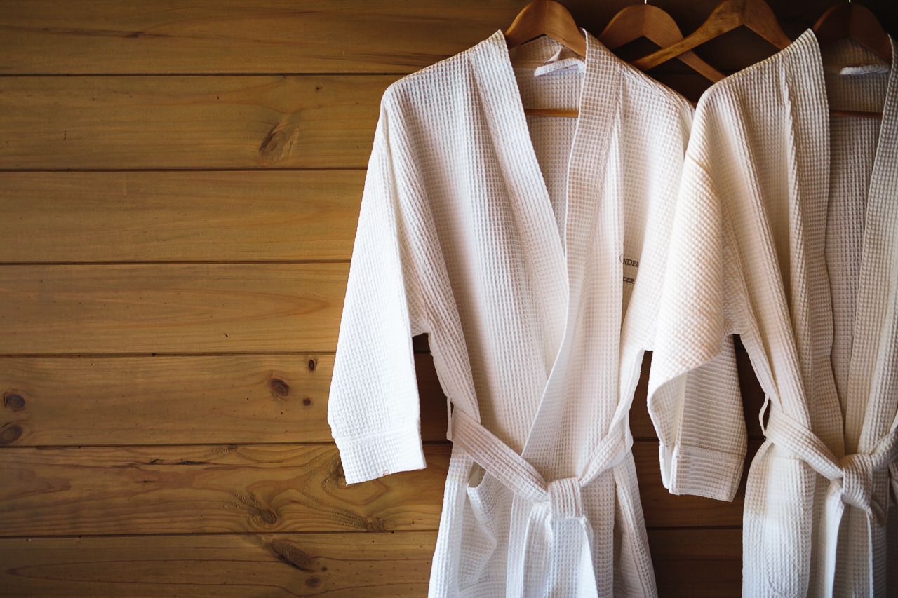 Two white robes hanging on wooden hangers against a wooden wall.