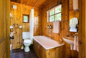 Un baño de cabaña de madera con inodoro, bañera, lavamanos y ventana.