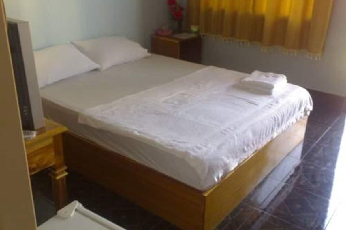 Una cama bien hecha en una habitación de hotel, con un cabecero de madera, una mesita de noche pequeña y una mesita auxiliar.