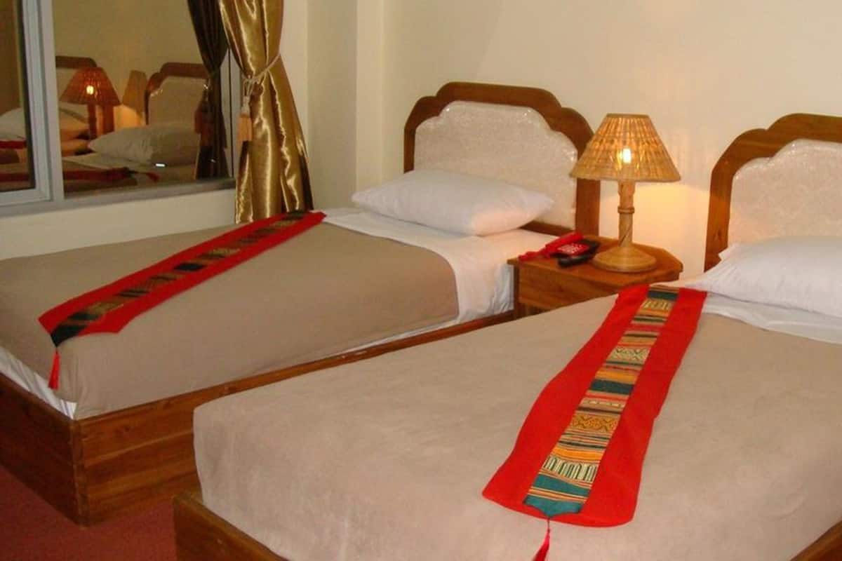 Dos camas contiguas con cabeceros de madera, ropa de cama blanca y detalles decorativos rojos.