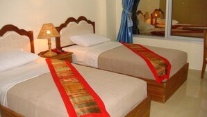 Twee eenpersoonsbedden met houten hoofdborden, wit beddengoed en rode decoratieve lopers.