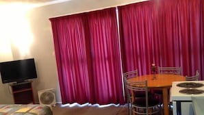 A room with a dining table, chairs, a TV, a fan, and a bed with a quilt. - Camberley Court Motel (Hastings)