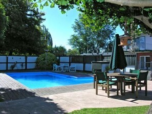 Un patio trasero con piscina, una mesa de patio con sillas y una silla colgante.