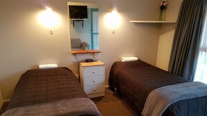 A hotel room with two beds, a small dresser, a mirror, a TV, and a shelf with a vase. - Camberley Court Motel (Hastings)
