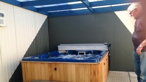A hot tub with a wooden exterior and a metal frame, situated outdoors with a covered area overhead. - Camberley Court Motel (Hastings)