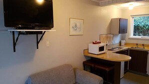 A compact living space with a flat-screen TV mounted on the wall, a kitchenette with a microwave, and a sofa. - Camberley Court Motel (Hastings)
